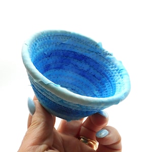 May include: A small blue and white fabric bowl with a quilted design. The bowl is made of layers of fabric sewn together to create a unique and textured look.