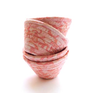 May include: A stack of three pink fabric bowls with a white floral pattern. The bowls are made of a soft, quilted fabric and are perfect for holding small items.