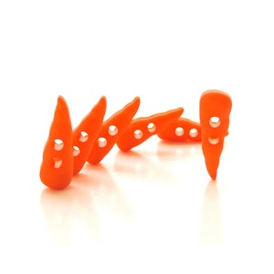 May include: A row of five orange carrot-shaped buttons with two holes each. The buttons are arranged in a line, with the last button standing upright.