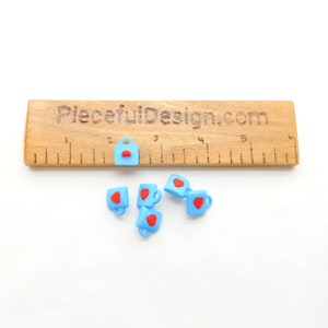 May include: Light blue miniature mugs and a small bag charm with red heart accents. The charms are arranged near a wooden ruler with the text "PiecefulDesign.com". These charms are ideal for crafting and jewelry making.