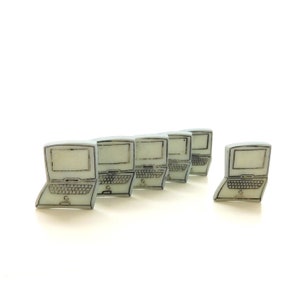 May include: A collection of small, off-white laptop-shaped objects with black outlines. The laptops are arranged in a row, with one slightly offset. The screens are blank, and the keyboards are detailed. The objects are on a white background.