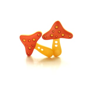 May include: Two red and yellow mushroom-shaped buttons with white polka dots. The buttons are made of plastic and have a glossy finish.