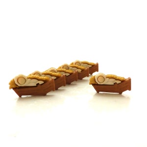 May include: A row of six brown wooden mangers with a yellow hay-like material and a white baby doll inside each manger.