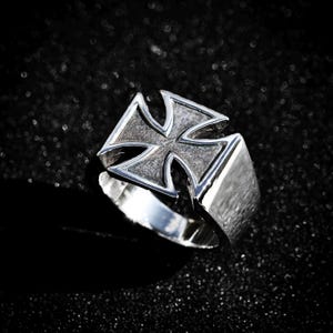 Könnte beinhalten: Ein silberner Ring mit einem erhabenen, strukturierten Eisernen Kreuz-Design.