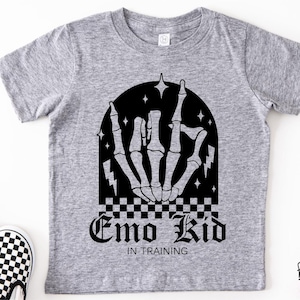 May include: A gray t-shirt with a black graphic of a skeleton hand making a rock-and-roll gesture. The text "Emo Kid In Training" is below the hand. A pair of black and white checkered slip-on shoes are visible.