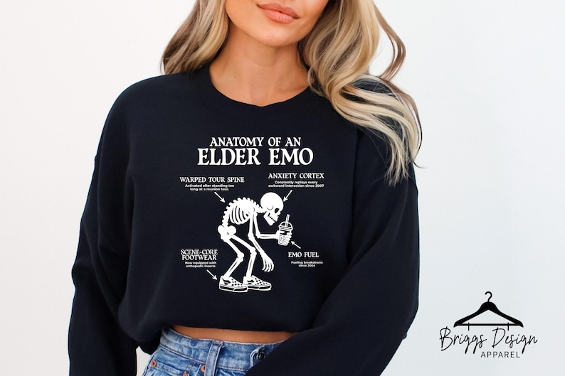 May include: Black sweatshirt with the text "ANATOMY OF AN ELDER EMO" and a skeleton graphic. The graphic includes labels for "WARPED TOUR SPINE", "ANXIETY CORTEX", "SCENE CORE FOOTWEAR", and "EMO FUEL". The sweatshirt is from Briggs Design Apparel.