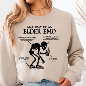 May include: Beige sweatshirt with the text "ANATOMY OF AN ELDER EMO" and a black skeleton graphic. The graphic includes labels for "WARPED TOUR SPINE", "ANXIETY CORTEX", "SCENE-CORE FOOTWEAR", and "EMO FUEL".