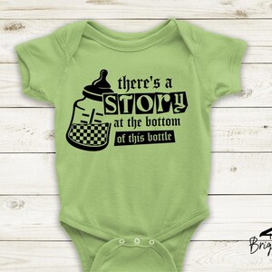May include: Light green baby onesie with a black graphic of a baby bottle and the text "there's a STORY at the bottom of this bottle." The onesie has short sleeves and snaps at the bottom. Briggs Design Apparel logo is at the bottom.