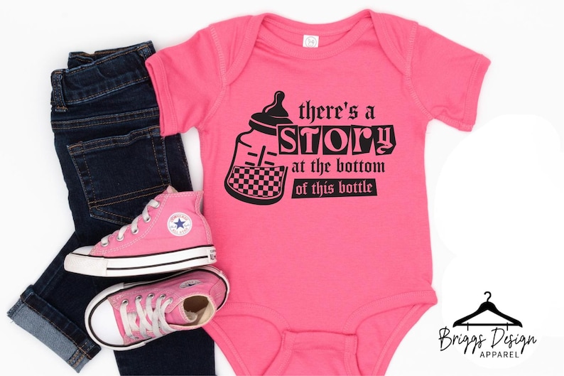 May include: A pink baby onesie with the text "there's a STORY at the bottom of this bottle" and a bottle graphic. The onesie is paired with dark blue jeans and pink high-top sneakers.