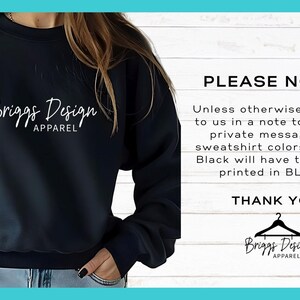 May include: A navy blue sweatshirt with the white text "Briggs Design Apparel" on the front. The image also includes a note stating that all sweatshirt colors except black will have the design printed in black.