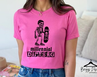 May include: A bright pink t-shirt featuring a black graphic of a skeleton wearing a beanie and holding a skateboard. The skateboard has a skull and crossbones design. The text "millennial DIRT BAG" is below the graphic.