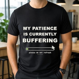 Op de afbeelding: Een zwart t-shirt met korte mouwen voorzien van de witte tekst MY PATIENCE IS CURRENTLY BUFFERING boven een laadbalkgrafiek met een cursorpictogram en de kleinere witte tekst please do not refresh met een reeks stippen eronder.