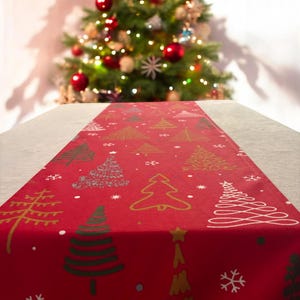 Puede incluir: Caminero de mesa rojo con un patrón de árbol de Navidad. El camino de mesa está decorado con árboles y copos de nieve dorados, verdes y blancos.