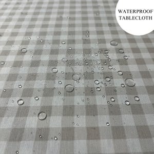 May include: A close-up of a white and gray gingham tablecloth with water droplets on the surface. The text "WATERPROOF TABLECLOTH" is visible in the upper right corner of the image.