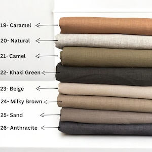 Op de afbeelding: Een stapel van acht stofstalen in verschillende tinten bruin, beige en grijs. De stalen zijn gelabeld met nummers en kleurennamen, waaronder Caramel, Natuurlijk, Camel, Khaki Groen, Beige, Melkbruin, Zand en Anthraciet.