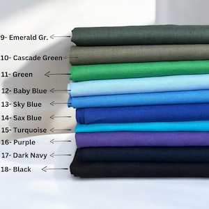 Op de afbeelding: Een stapel stofstalen in verschillende kleuren, waaronder smaragdgroen, cascadegroen, groen, babyblauw, hemelsblauw, saxblu, turquoise, paars, donkerblauw en zwart. De stalen zijn genummerd en met de kleurnaam gelabeld.