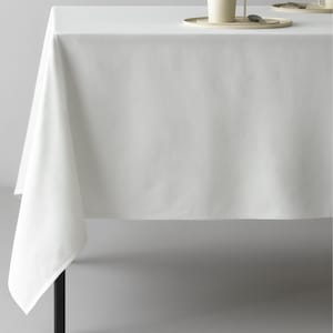 Può includere: Una tovaglia bianca copre un tavolo, con un angolo del tessuto che pende. Due tazze e piattini color crema con cucchiaini sono sul tavolo. Le gambe del tavolo sono nere.
