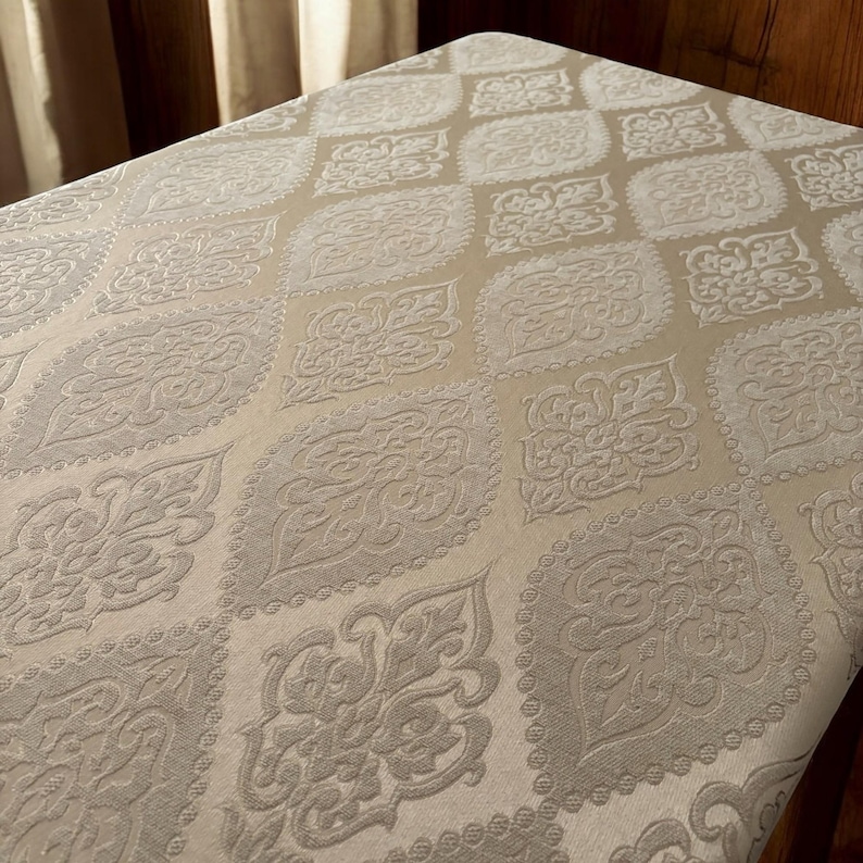 Puede incluir: Primer plano de una tela beige con un patr&oacute;n en relieve de diamantes blancos y dise&ntilde;os florales. La tela tiene un tacto suave y texturizado.