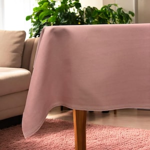 May include: A dusty rose tablecloth with a subtle sheen. The tablecloth is draped over a table with a wooden leg.
