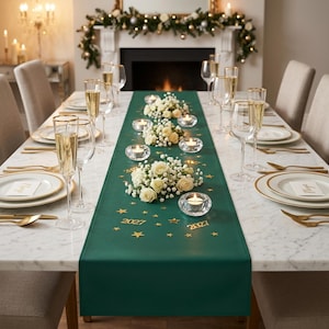 Op de afbeelding: Een feestelijk gedekte eettafel. De tafel heeft een groene tafelloper met gouden sterren en de cijfers "2021" en "2027". Witte rozen en kaarsen zijn langs de loper geplaatst. Champagneglazen en couverts met gouden randen maken het elegante geheel af.