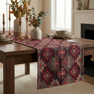 May include: A patterned table runner with a geometric design in shades of red, green, and brown. The runner is placed on a dark wooden table, with candles, vases, and tableware visible.