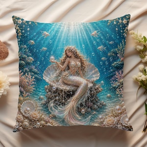 May include: A square throw pillow featuring a detailed underwater scene with a mermaid sitting on a large open seashell. The mermaid has long flowing hair and a shimmering tail, surrounded by coral, small fish, bubbles, and scattered pearls.