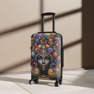 Puede incluir: Una maleta negra con ruedas que presenta un estampado gráfico vibrante y colorido de una persona con patrones intrincados y arremolinados en tonos azul, naranja, rojo y amarillo alrededor de la cabeza. Tiene un asa negra y cuatro ruedas.