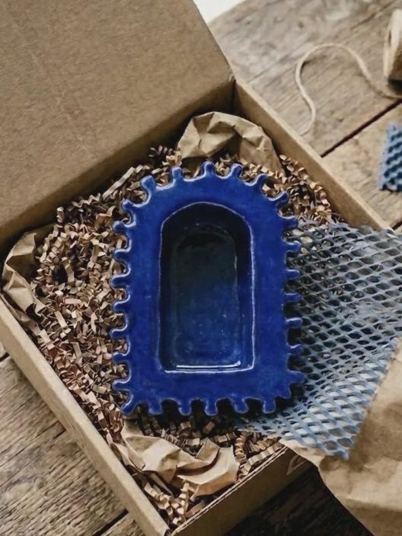 Pu&ograve; includere: Un vassoio in ceramica blu profondo con un centro rettangolare e un bordo smerlato e ondulato. L'oggetto presenta una finitura lucida e liscia con una conca incassata, presentato in una scatola di cartone con riempitivo di carta marrone.