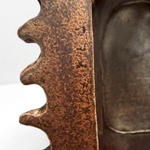 Pu&ograve; includere: Un oggetto in metallo testurizzato color bronzo con una serie di sporgenze prominenti, frastagliate e simili a denti lungo un bordo. La superficie ha un aspetto usurato e maculato con toni marrone scuro e rame, e una profonda cavit&agrave; interna.