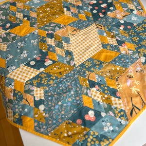 May include: A yellow and green patchwork quilt with a geometric pattern. The quilt is made of various fabrics with floral and geometric designs.