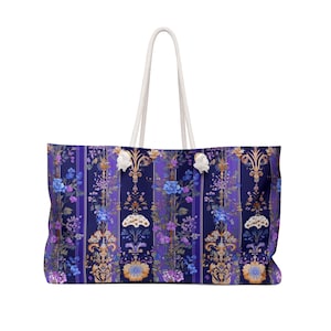 Könnte beinhalten: Eine gestreifte Tragetasche in Lila und Weiß mit einem Blumenmuster. Die Tasche hat weiße Kordelgriffe.