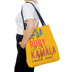 Op de afbeelding: Een gele tote bag met een blauw, rood en roze grafisch ontwerp met de tekst "USA say, so RUBY could walk, so KAMALA could run!"