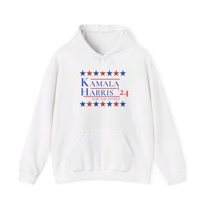 Op de afbeelding: Witte hoodie met een voorzak en een trekkoord. De voorkant toont de tekst "KAMALA HARRIS '24" in blauw en rood, met sterrenafbeeldingen erboven en eronder. De zin "FOR THE PEOPLE" staat eronder.