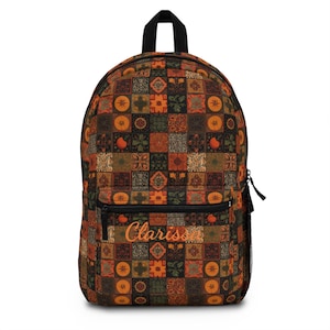 May include: A backpack with a colorful patchwork pattern in shades of brown, orange, and green. The backpack has a black top handle, a front pocket with a zipper, and the name "Clarissa" in orange script.