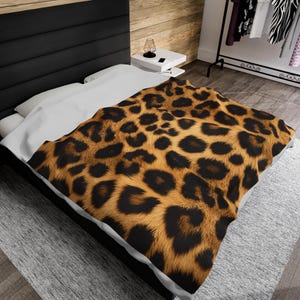 Puede incluir: Una colcha de cama de estampado de leopardo marrón y negro con una sábana blanca debajo. La colcha está sobre una cama con una cabecera negra.