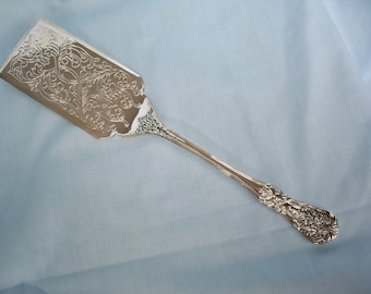 May include: A silver cake server with an ornate, floral design. The handle is also decorated with a floral pattern.