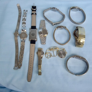 May include: A collection of various wristwatches, showcasing diverse styles and designs. The watches feature metal bands in silver and gold tones, along with leather straps. The assortment includes both analog and digital watch faces, offering a range of options for personal style.