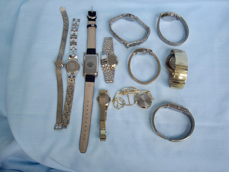 May include: A collection of various wristwatches, showcasing diverse styles and designs. The watches feature metal bands in silver and gold tones, along with leather straps. The assortment includes both analog and digital watch faces, offering a range of options for personal style.