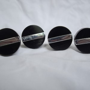 May include: Four black round knobs with a silver stripe across the center.