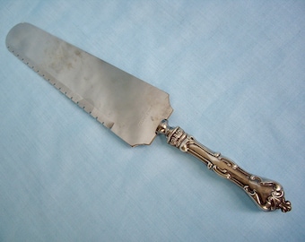 May include: Silver cake server with a serrated edge and an ornate handle. The blade is marked "STAINLESS".