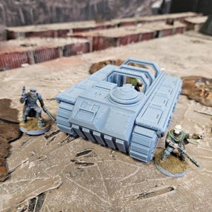 Puede incluir: Un tanque de juguete azul claro con un diseño detallado, con orugas y una torreta. Dos figuras en miniatura, una de ellas sosteniendo un arma, están cerca sobre una superficie texturizada. La escena evoca un tema militar o de juego de guerra.