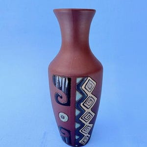 May include: A terracotta vase with a geometric design in black, white, and blue. The vase has a narrow neck and a wide base.