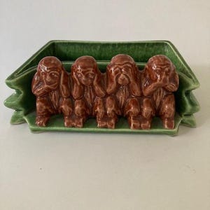 May include: A green ceramic planter with four brown monkeys in a row. The monkeys are covering their eyes, ears, and mouths. The planter is shaped like a leaf.