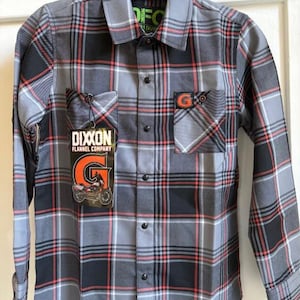 May include: Gray, black, and red plaid flannel shirt with two chest pockets. The shirt has a button-down front and long sleeves. A tag with the words "DIXXON FLANNEL COMPANY" and a motorcycle graphic is attached to the shirt.