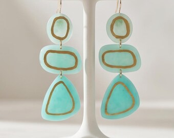 Pendientes colgantes hechos a mano de arcilla polimérica turquesa con detalles geométricos dorados de inspiración costera.