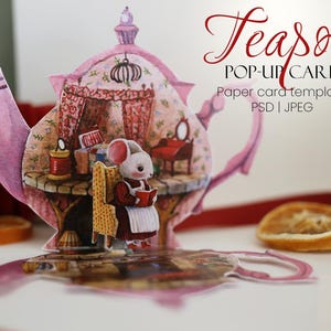 Puede incluir: Tarjeta desplegable rosa con forma de tetera, con una escena interior detallada y un ratón leyendo un libro. La tarjeta incluye el texto "Teasot POP-UP CARD" y es una plantilla de tarjeta de papel.