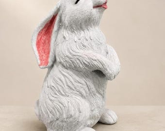 May include: A white rabbit figurine standing upright with its front paws tucked against its chest. The rabbit has closed eyes, a small pink nose, and a pink inner ear. The textured surface mimics fur, and the figure is captured in a side profile view.