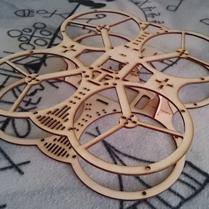 May include: A wooden frame for a drone, with four circular openings for propellers. The frame is made of light brown wood and has a textured surface.