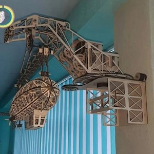 Puede incluir: Un modelo de madera de un dirigible steampunk que es levantado por una grúa con engranajes y un sistema de poleas. El modelo está hecho de madera cortada con láser y está montado en una pared.