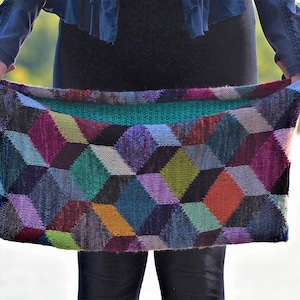 Op de afbeelding: Een kleurrijke gebreide sjaal met een geometrisch patroon van kubussen in tinten van paars, turquoise, groen, oranje en bruin.